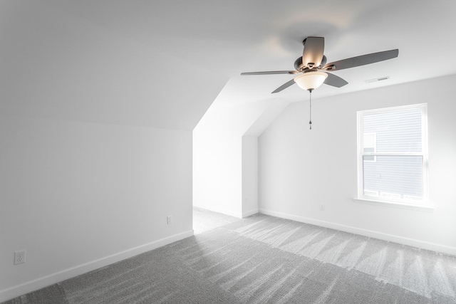 additional living space with carpet flooring, vaulted ceiling, visible vents, baseboards, and ceiling fan