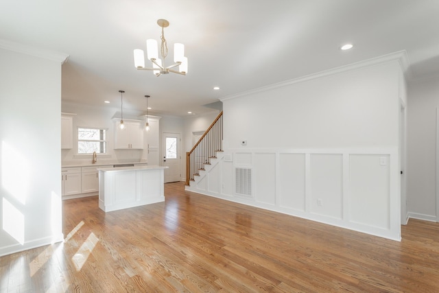 kitchen with an inviting chandelier, visible vents, a decorative wall, crown molding, and a center island