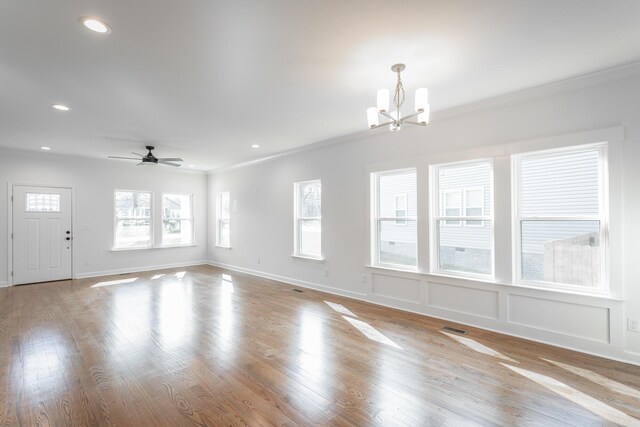 unfurnished living room with recessed lighting, wood finished floors, ornamental molding, and ceiling fan with notable chandelier