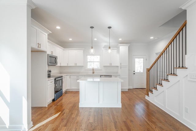 kitchen featuring stainless steel appliances, light wood-style flooring, white cabinetry, light countertops, and ornamental molding