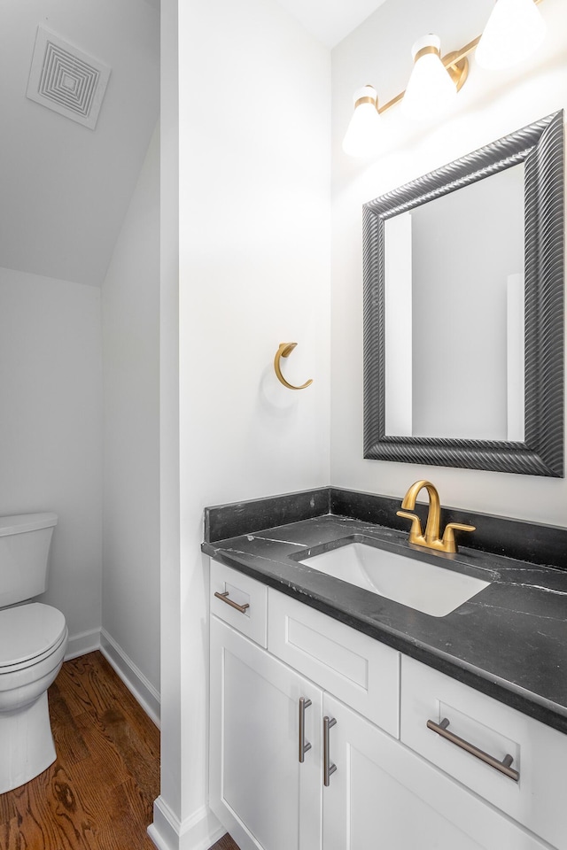 half bathroom with wood finished floors, visible vents, toilet, vanity, and baseboards