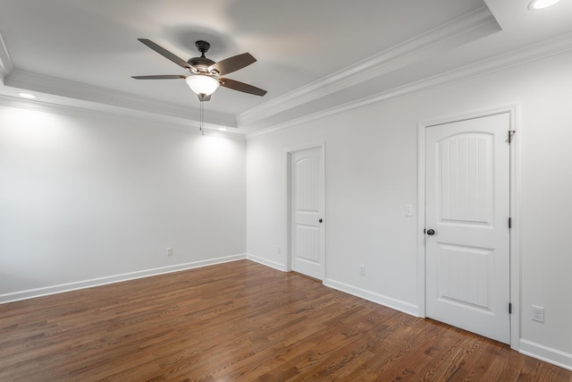 empty room featuring a ceiling fan, crown molding, wood finished floors, a tray ceiling, and baseboards