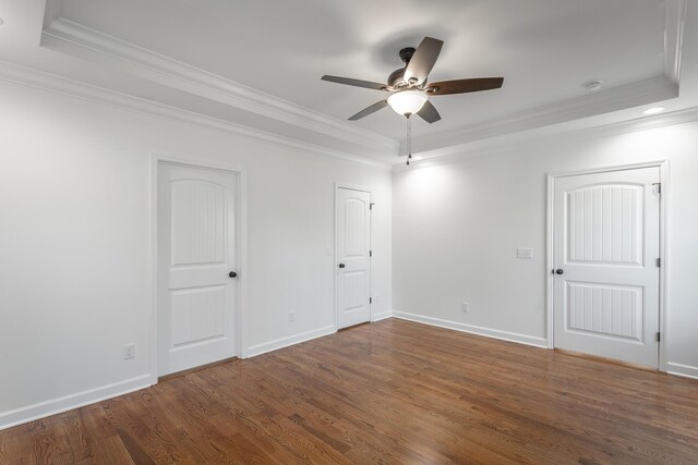unfurnished bedroom featuring a tray ceiling, wood finished floors, crown molding, and baseboards