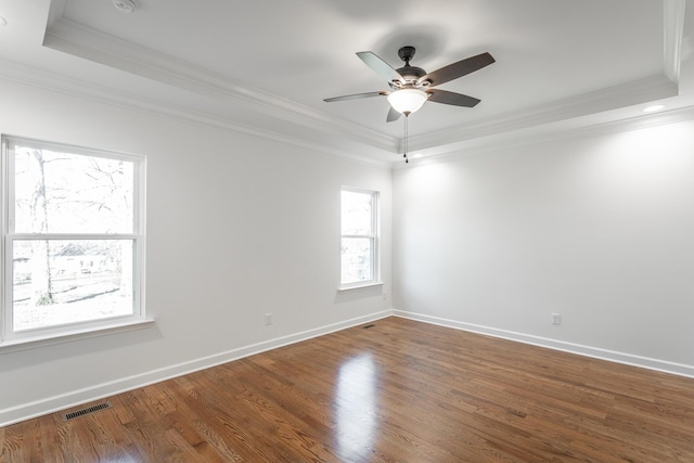 unfurnished room with a tray ceiling, wood finished floors, visible vents, and ornamental molding