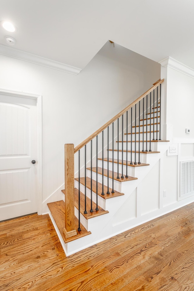 staircase with wood finished floors, visible vents, and ornamental molding