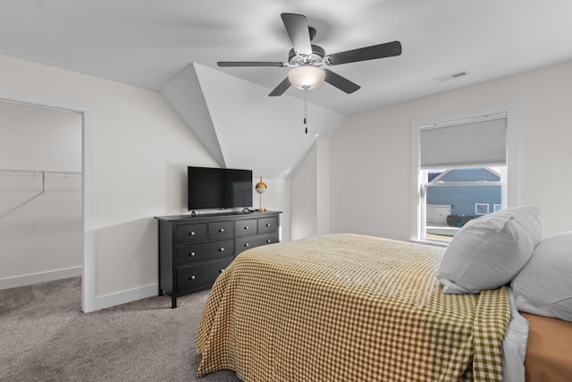 carpeted bedroom featuring a ceiling fan, a walk in closet, lofted ceiling, baseboards, and visible vents