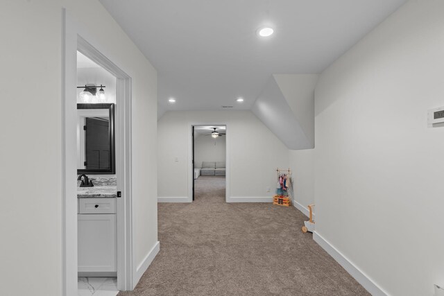 hallway featuring baseboards, recessed lighting, lofted ceiling, a sink, and light colored carpet