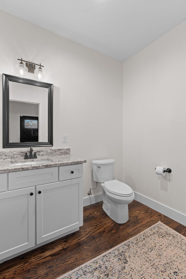 bathroom featuring toilet, vanity, baseboards, and wood finished floors