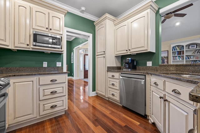 kitchen featuring crown molding, a ceiling fan, appliances with stainless steel finishes, dark wood-style floors, and cream cabinets
