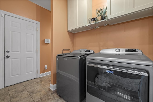 clothes washing area featuring light tile patterned floors, cabinet space, baseboards, and washer and clothes dryer