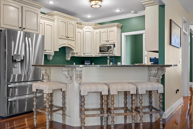 kitchen featuring cream cabinetry, stainless steel appliances, a breakfast bar, and dark wood finished floors