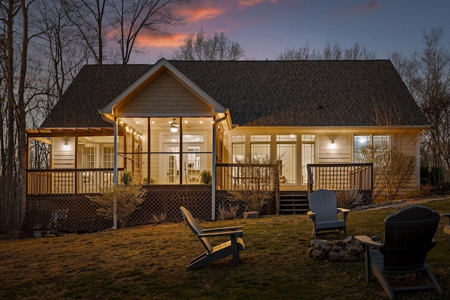 back of property at dusk with a lawn, roof with shingles, and a deck