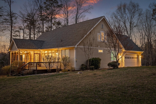 property exterior at dusk featuring a shingled roof, a garage, and a yard