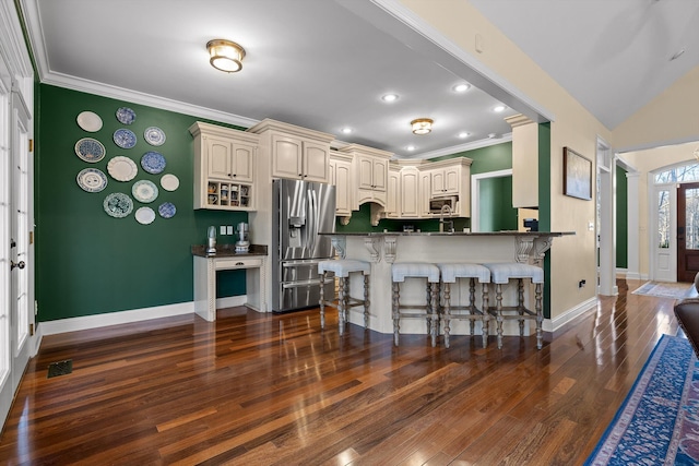 kitchen with cream cabinetry, ornamental molding, appliances with stainless steel finishes, dark wood-style floors, and a kitchen breakfast bar