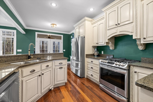 kitchen featuring ornamental molding, stainless steel appliances, dark stone counters, dark wood-type flooring, and a sink