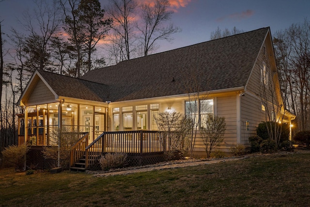 rear view of property with roof with shingles, a sunroom, and a yard