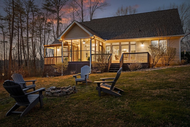 playground at dusk with a fire pit, a wooden deck, a sunroom, and a yard