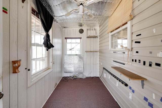 interior space with carpet floors, wood walls, and a ceiling fan