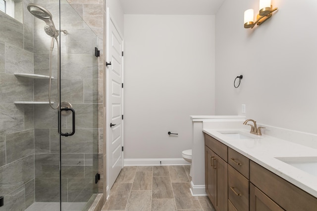 bathroom featuring toilet, baseboards, a shower stall, a sink, and double vanity