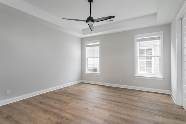 empty room with wood finished floors, a tray ceiling, baseboards, and visible vents