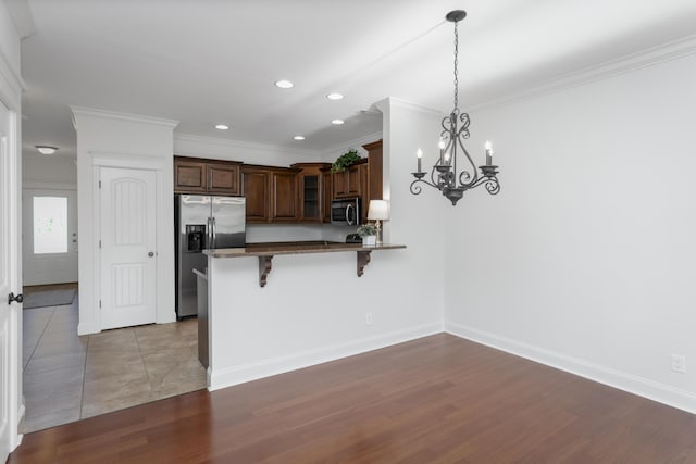 kitchen featuring a breakfast bar, appliances with stainless steel finishes, a peninsula, glass insert cabinets, and ornamental molding