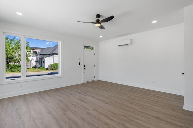 unfurnished room with baseboards, a wall mounted AC, wood finished floors, and a ceiling fan