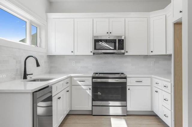kitchen featuring light countertops, tasteful backsplash, stainless steel appliances, a sink, and light wood-style floors