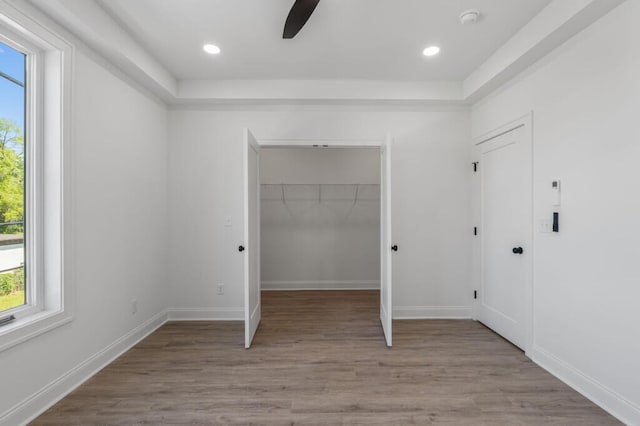 unfurnished bedroom featuring baseboards, recessed lighting, wood finished floors, and a walk in closet