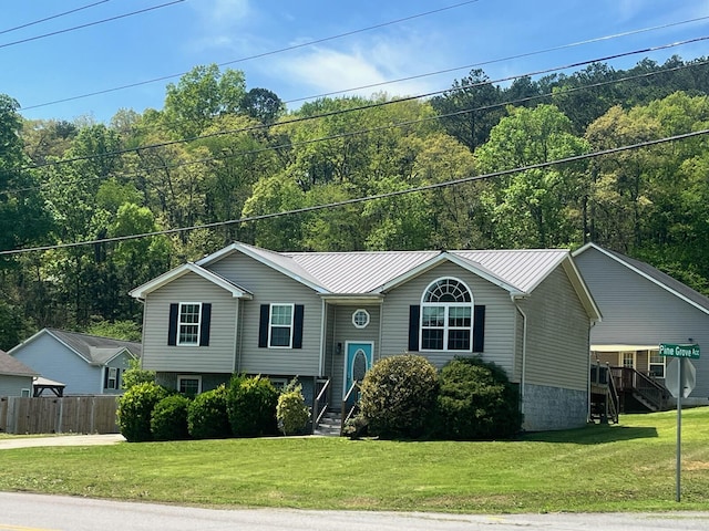 split foyer home with fence, metal roof, a front lawn, and a wooded view