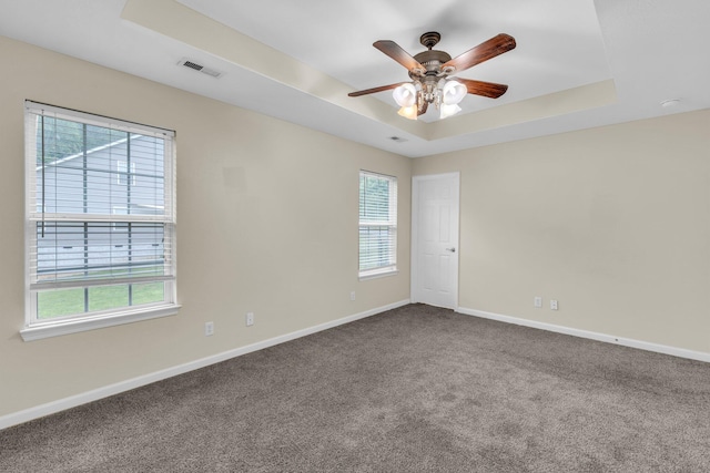 spare room with a raised ceiling, plenty of natural light, dark colored carpet, and visible vents
