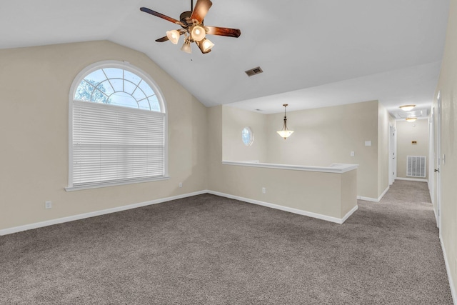empty room featuring a ceiling fan, lofted ceiling, dark carpet, and visible vents
