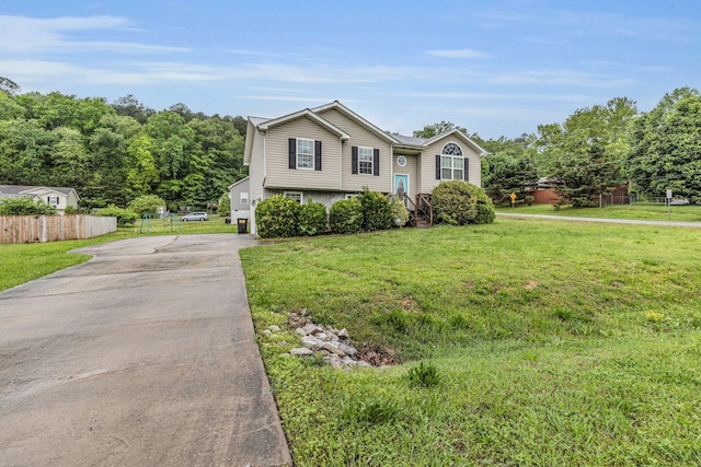 raised ranch featuring fence, a garage, driveway, and a front yard