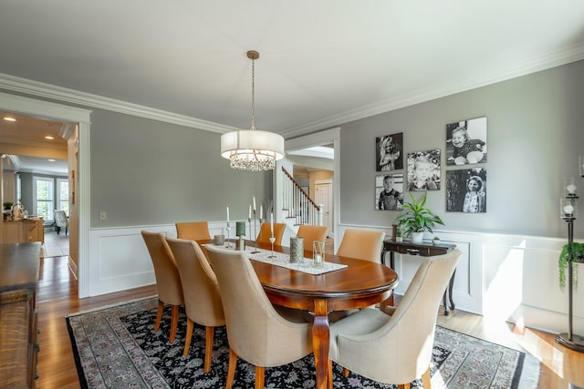 dining space featuring ornamental molding, an inviting chandelier, stairway, a wainscoted wall, and wood finished floors