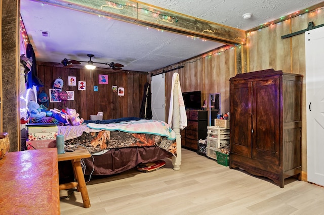bedroom featuring wood finished floors, wooden walls, a barn door, and a textured ceiling