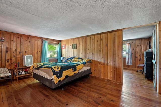 bedroom with a textured ceiling, wooden walls, and hardwood / wood-style flooring