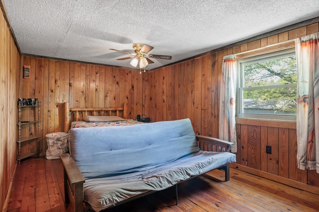 bedroom featuring ceiling fan, a textured ceiling, wood walls, and hardwood / wood-style floors