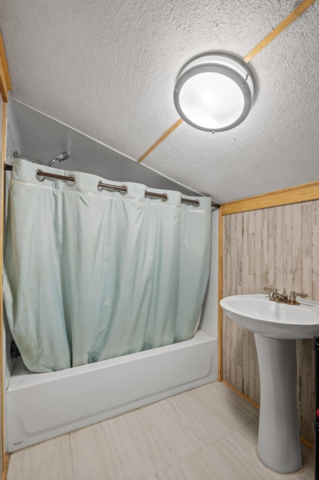 full bath with vaulted ceiling, a textured ceiling, shower / tub combo with curtain, and wooden walls