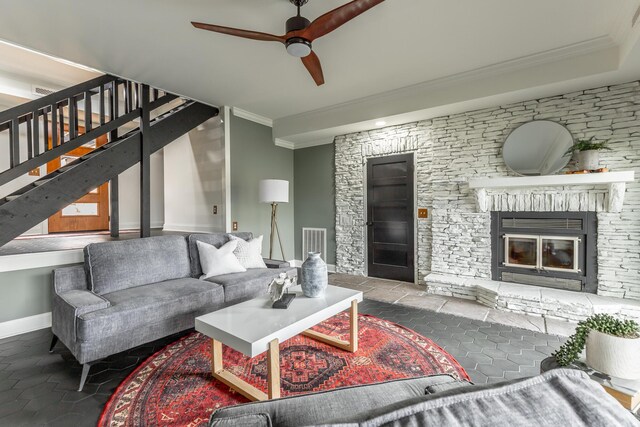 living room featuring crown molding, stairway, a glass covered fireplace, baseboards, and ceiling fan