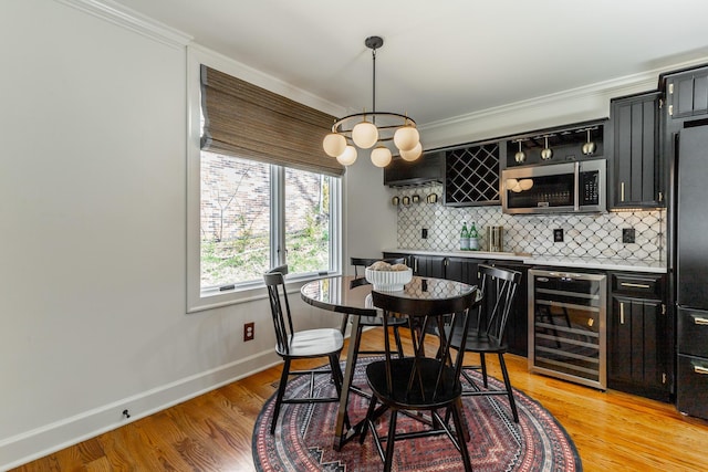 dining room with light wood-style flooring, baseboards, wet bar, and beverage cooler