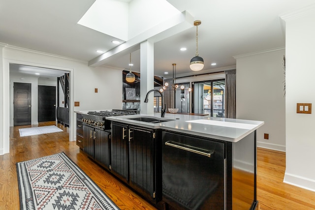 kitchen with light countertops, a sink, stainless steel gas stovetop, light wood-style floors, and ornamental molding