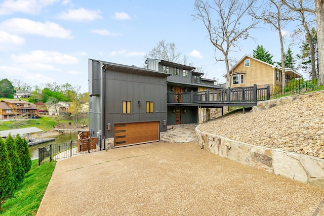 back of property with concrete driveway, fence, an attached garage, board and batten siding, and a water view