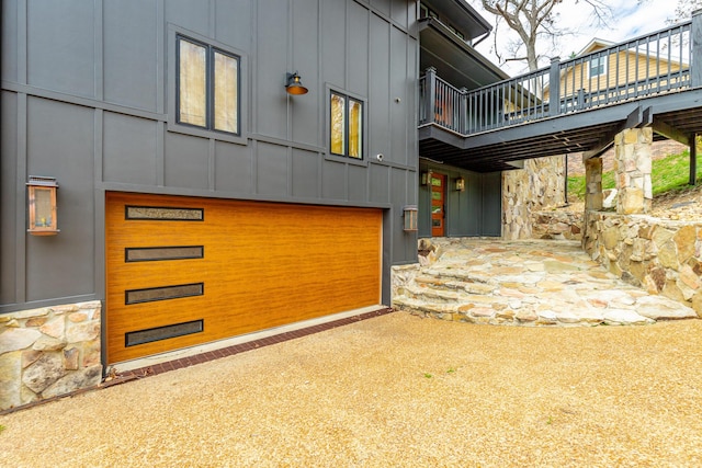 doorway to property with stone siding, board and batten siding, driveway, a deck, and a garage