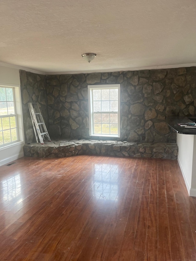 empty room with crown molding, a fireplace, a textured ceiling, wood-type flooring, and visible vents