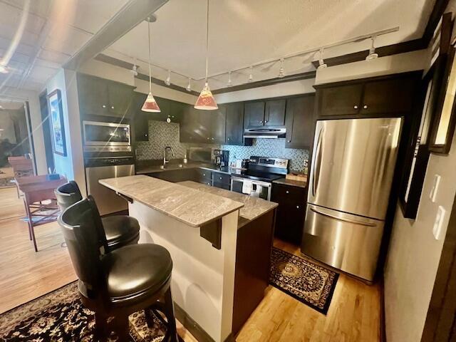 kitchen featuring track lighting, a kitchen island, under cabinet range hood, light wood-style flooring, and stainless steel appliances