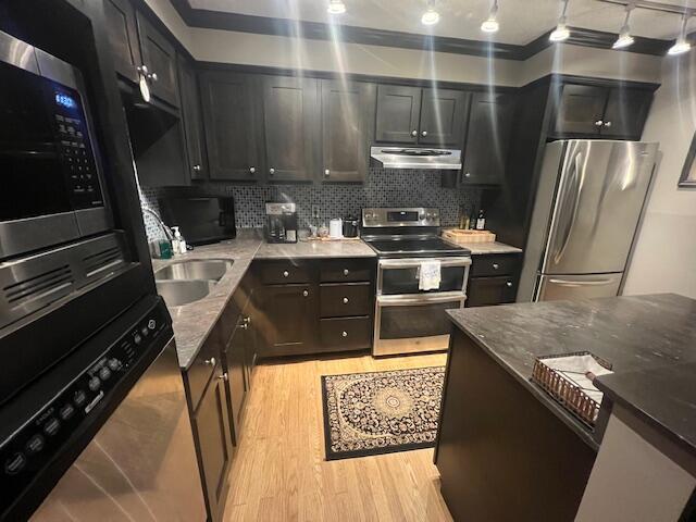 kitchen with decorative backsplash, exhaust hood, light wood finished floors, dark stone countertops, and stainless steel appliances