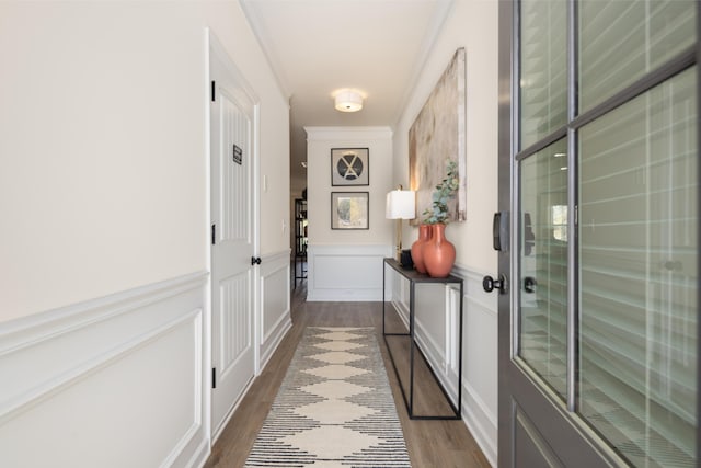 hall with wainscoting, crown molding, a decorative wall, and dark wood-type flooring