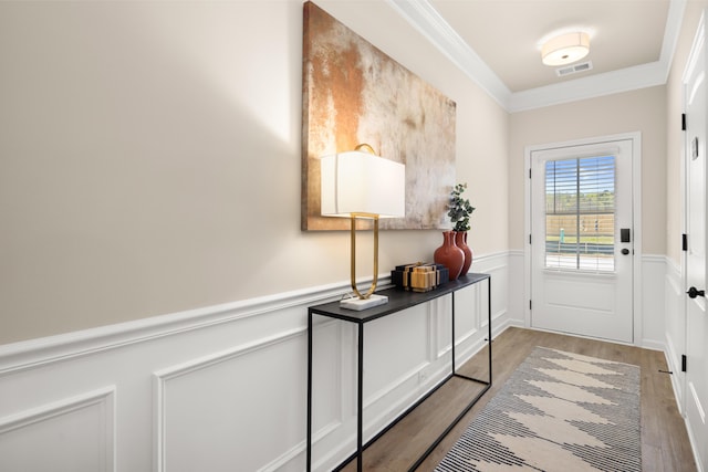 doorway with visible vents, crown molding, wood finished floors, and wainscoting