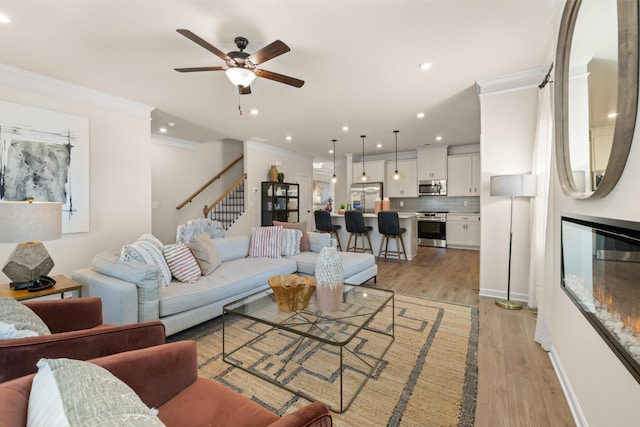 living room with stairs, a ceiling fan, light wood finished floors, ornamental molding, and recessed lighting