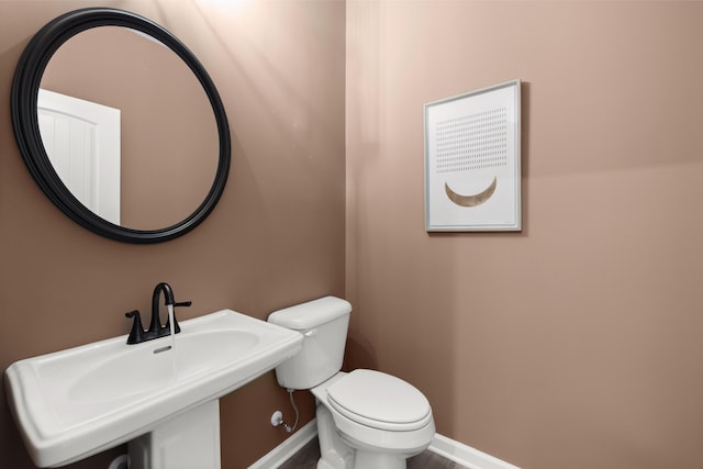 half bathroom featuring baseboards, a sink, and toilet
