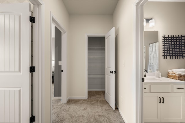 corridor with a sink, radiator, baseboards, and light colored carpet